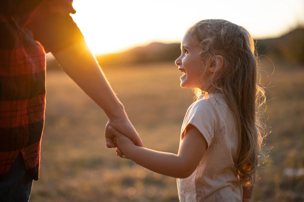 Niña pequeña de la mano de su madres en una puesta de sol