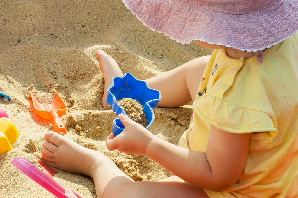 Niña pequeña con los pies descalzos al sol sobre la arena de la playa