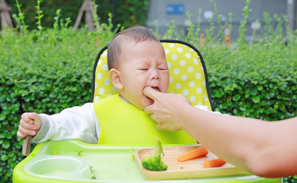 Bebé atragantándose mientras come con una mano adulta sacándole la comida de la boca