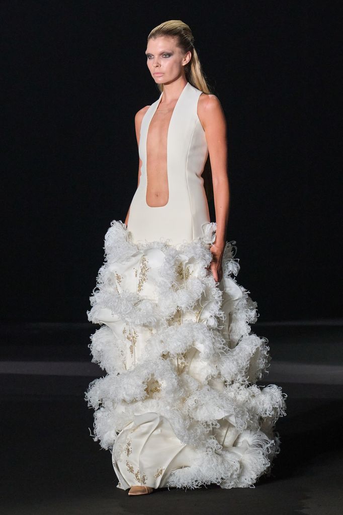 Modelo en pasarela con vestido blanco de plumas y escote profundo.