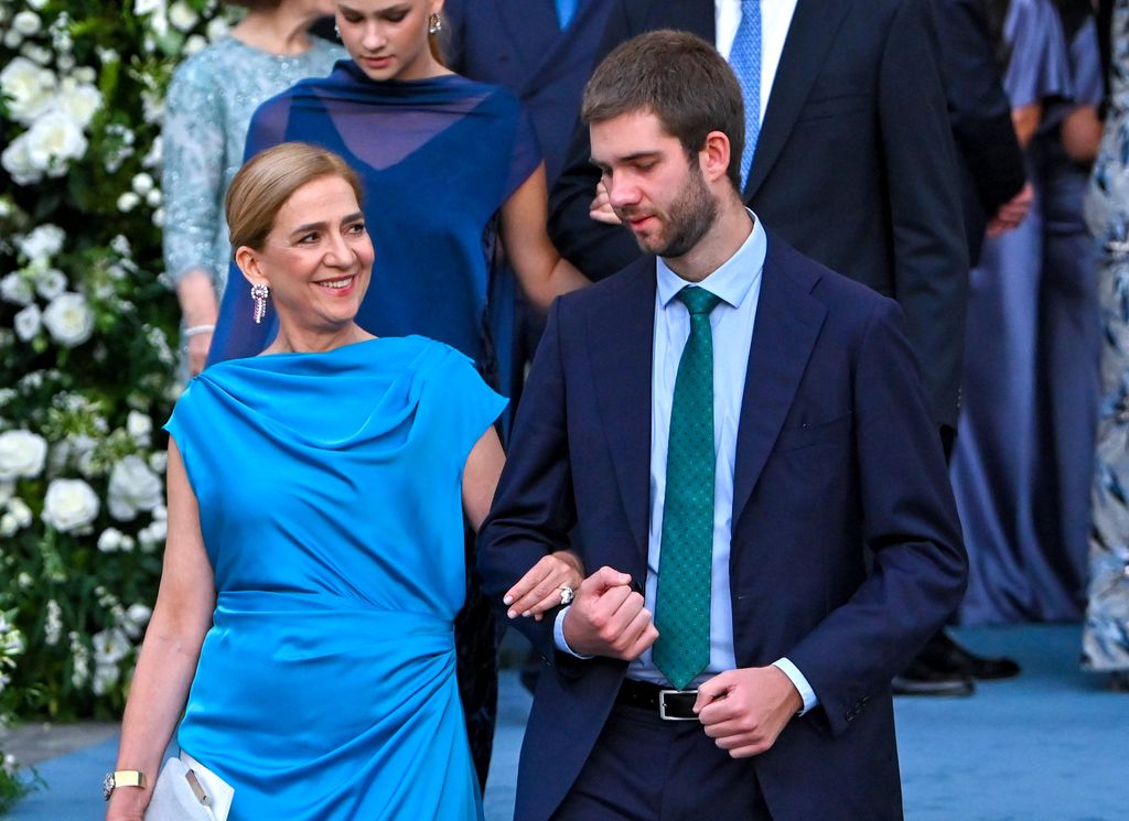Infanta Cristina en vestido azul y hombre en traje azul y corbata verde caminan juntos.