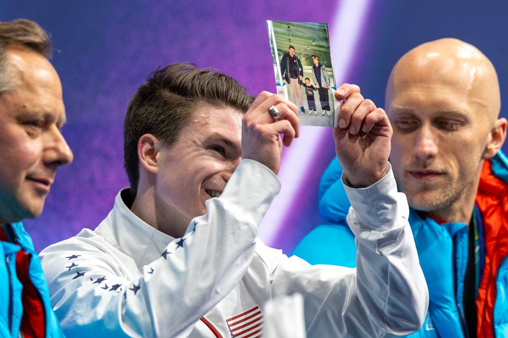 Maxim Naumov con una foto de sus padres mientras esperaba la puntuación de su rutina libre en los Juegos Olímpicos de Milano Cortina