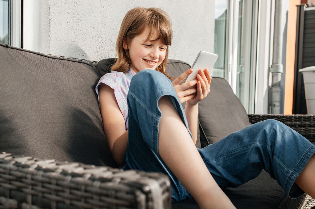 niña sentada en el sofá mirando su teléfono móvil