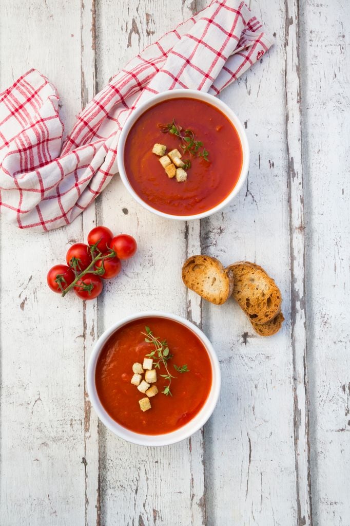 Dos cremas de tomate con pan tostado en una mesa gris