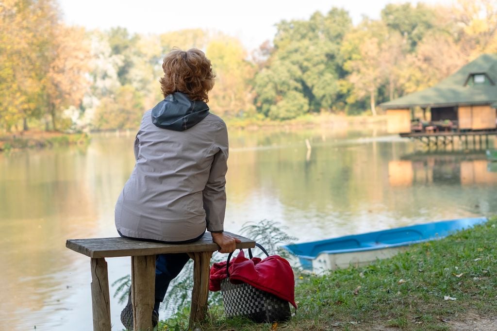mujer madura sentada en un banco mirando al horizonte, junto a un lago