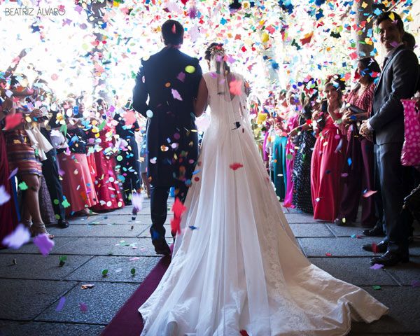 Pareja saliendo de boda con confeti cayendo. La mujer lleva un vestido blanco y el hombre un traje negro.