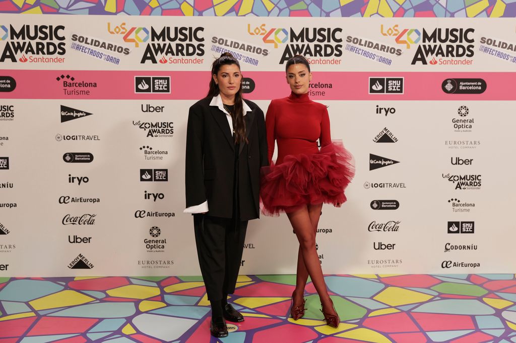 Plano entero de Alba Paul y Dulceida con traje negro y vestido rojo