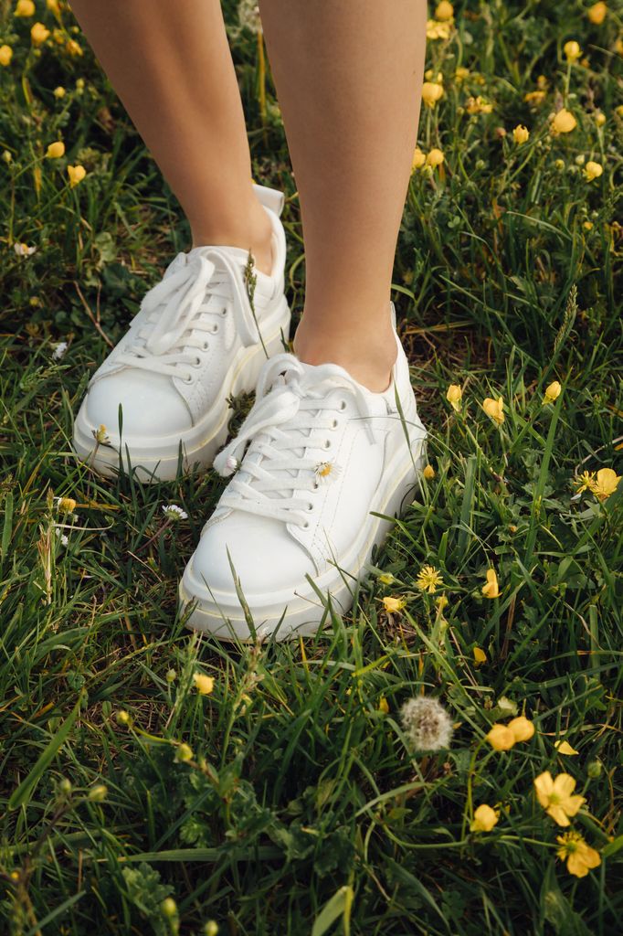 Zapatillas blancas sobre césped con flores amarillas
