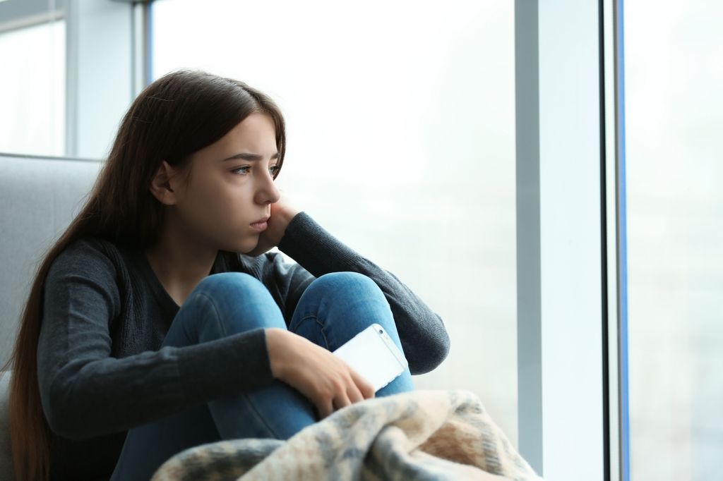 Chica adolescente mirando por la ventana con cara deprimida