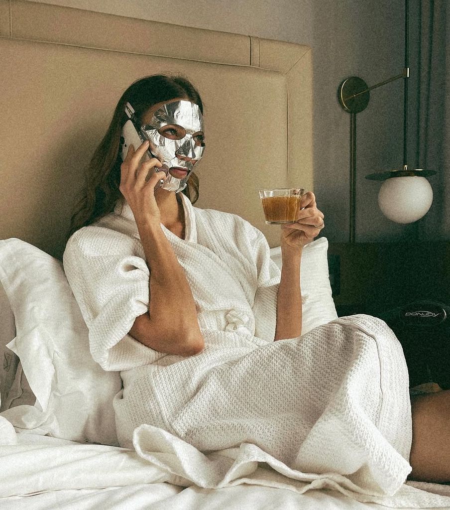 Karlie Kloss con el móvil tomándose un café con una mascarilla
