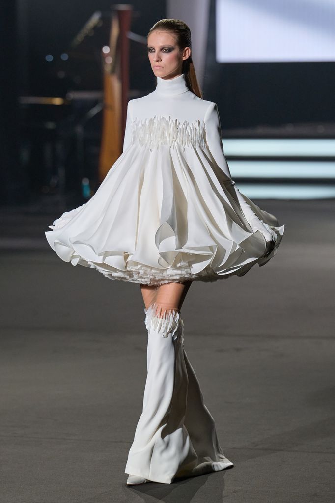 Modelo en pasarela con vestido blanco de mangas largas y falda voluminosa.