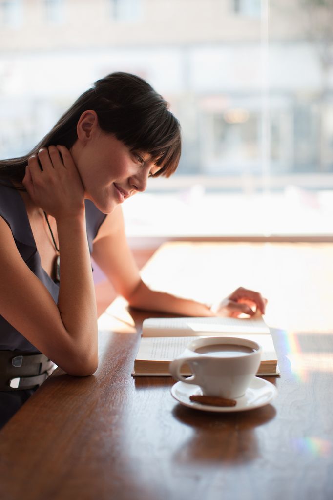 Mujer leyendo un libro con una taza de café en la mesa 