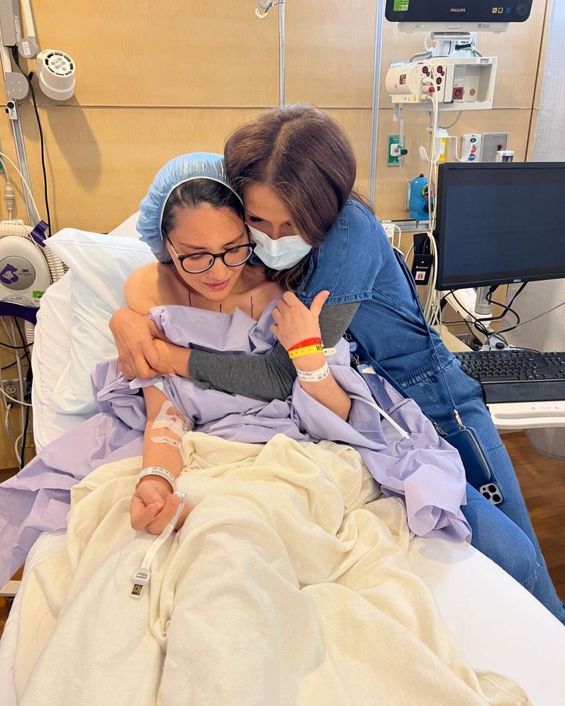 Olivia Munn en una camilla de hospital siendo abrazada en sus tratamientos de cáncer de mama