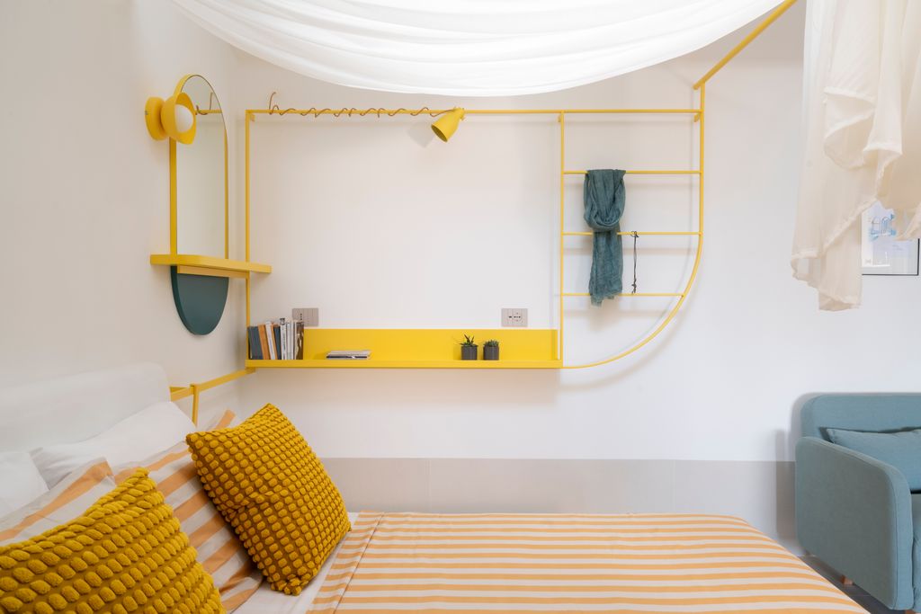 Mueble en hierro teñido de amarillo que alberga estantes abiertos, espejos, colgadores y hasta flexos y apliques