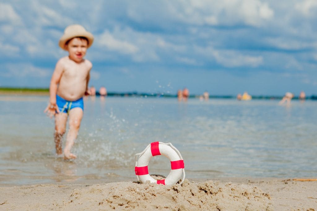 Niño pequeño jugando solo en la orilla de la playa con un salvavidas en primer plano para evitar ahogamientos