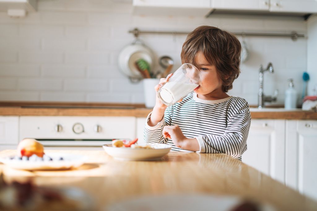 Niño desayunando un vaso de leche en su casa