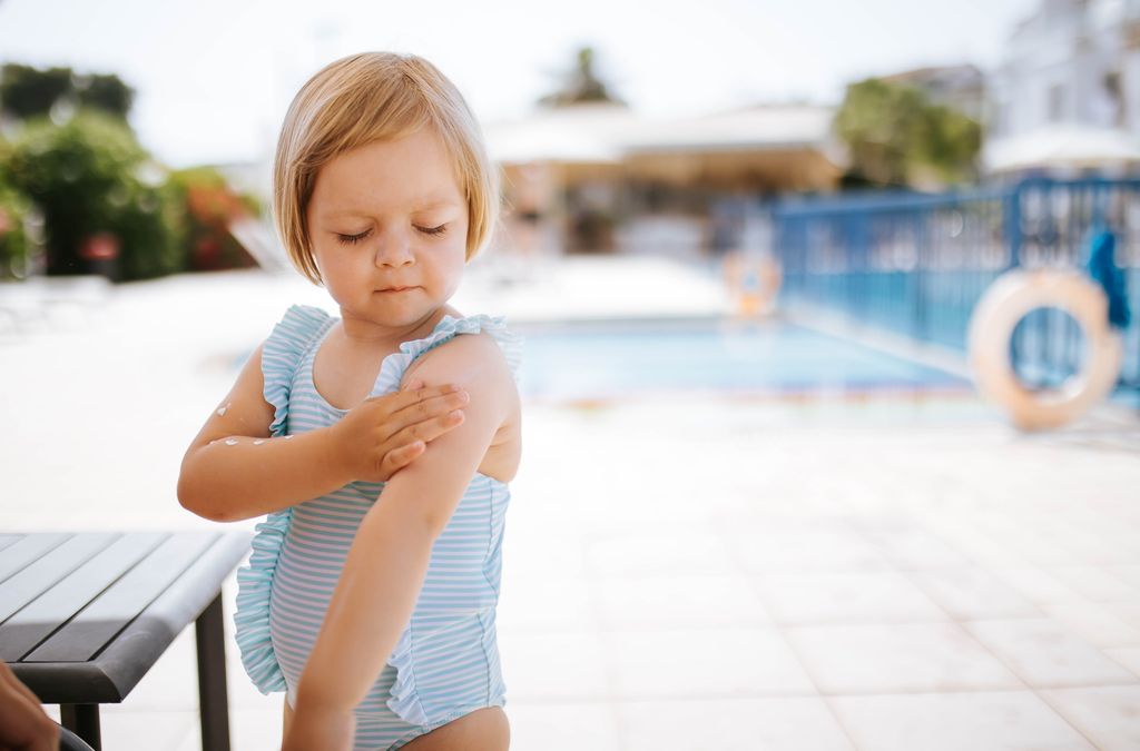 niña pequeña aplicándose crema solar en la piel, en verano, junto a una piscina