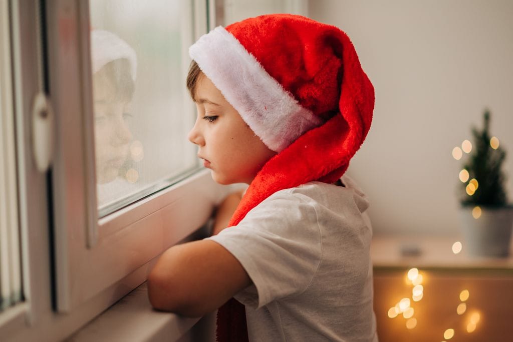 Niño con gorro de Navidad mirando triste por la ventana