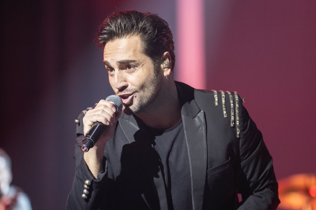 David Bustamante cantando en un escenario con traje negro y micrófono.