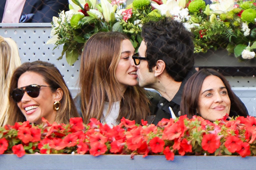 Cuatro personas, incluyendo a Macarena García, besan a un hombre con gafas. Están en un evento con flores.