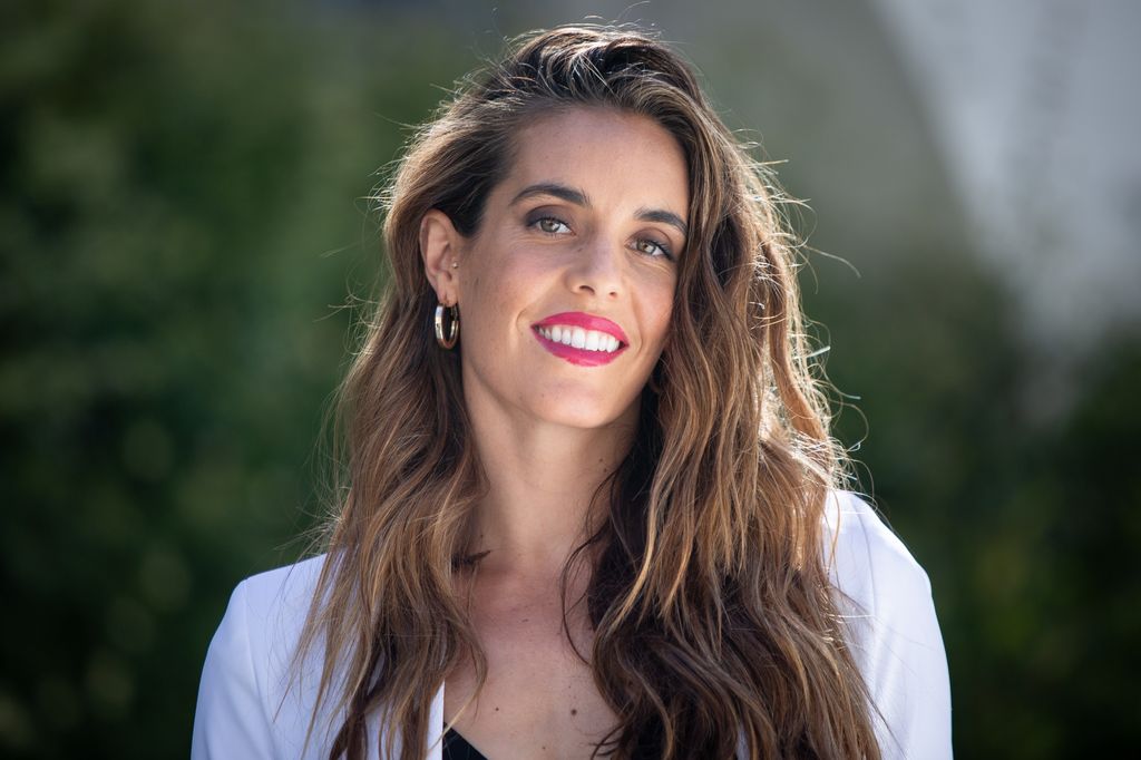 Ona Carbonell sonriendo con cabello largo y camisa blanca en exterior.