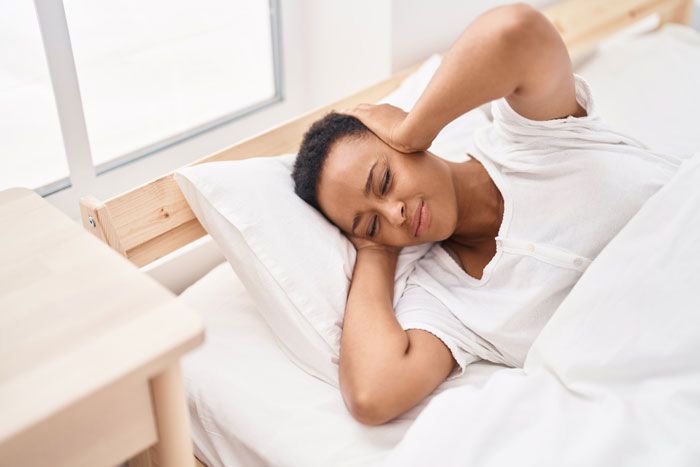 mujer tapándose los oídos en la cama