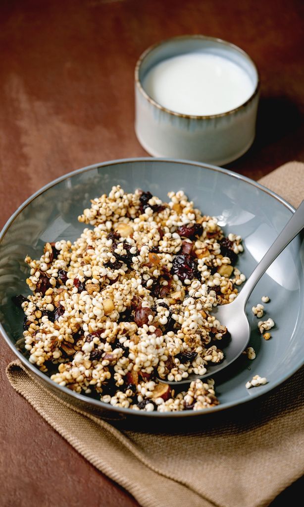 Homemade crunchy puffed millet grain granola with dried fruits and nuts in ceramic plate on textile napkin. cup of yogurt over brown texture background. Copy space. Healthy food breakfast