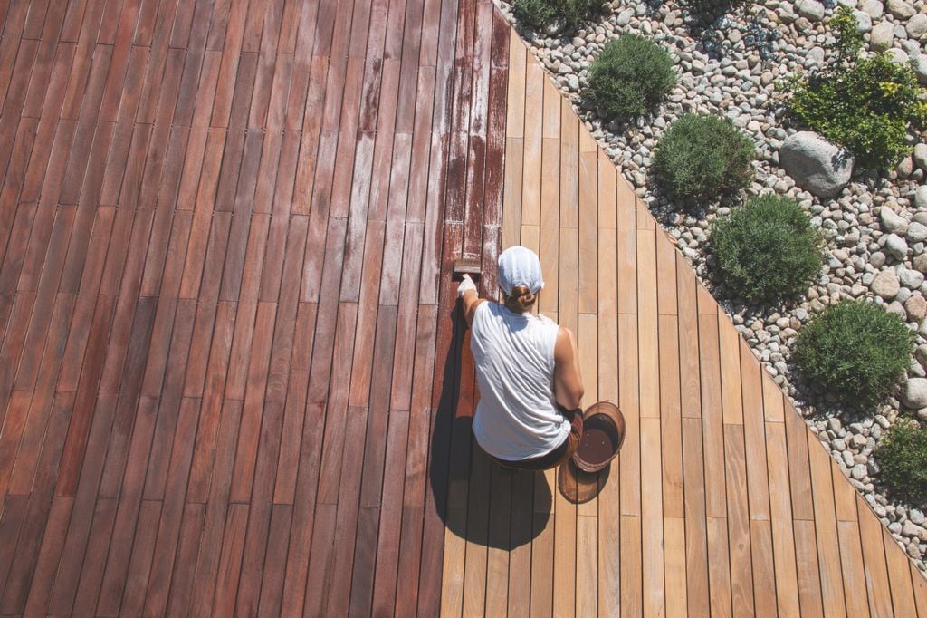 Mujer aplicando barniz a un suelo de tarima de madera de exterior