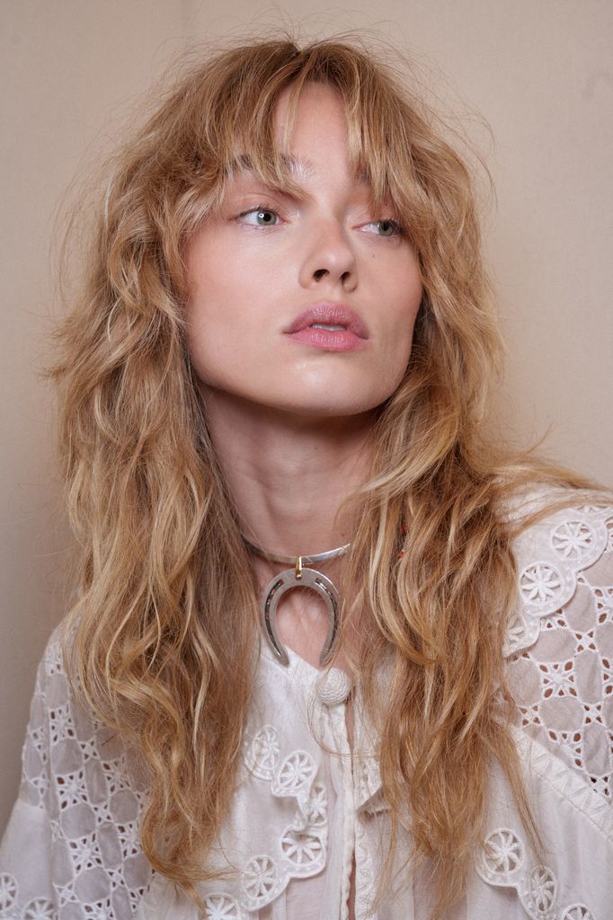 Modelo en backstage desfile Isabel Marant con camisa blanca, collar de herradura y pelo rubio con flequillo abierto
