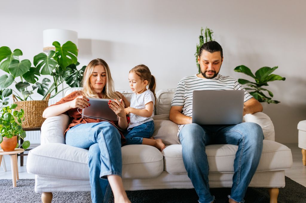 familia sentada en el sofá, usando pantallas