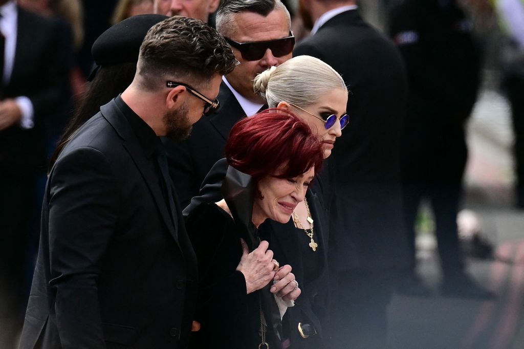 TOPSHOT - The family of Ozzy Osbourne, son Jack Osbourne (L), widow Sharon Osbourne (C) and daughter Kelly Osbourne (R) arrive to lay flowers at the Black Sabbath Bridge bench on Broad Street during a funeral procession for Ozzy Osbourne, the late lead singer of Black Sabbath, in Birmingham, central England on July 30, 2025. Thousands are expected to line the streets in Ozzy Osbourne's UK hometown of Birmingham on Wednesday to honour the heavy metal hell-raiser Ozzy Osbourne as he is laid to rest. Osbourne, nicknamed the "Prince of Darkness" and who once bit a bat while on stage while performing with his Black Sabbath band, died on July 22 at the age of 76. (Photo by Ben STANSALL / AFP) (Photo by BEN STANSALL/AFP via Getty Images)