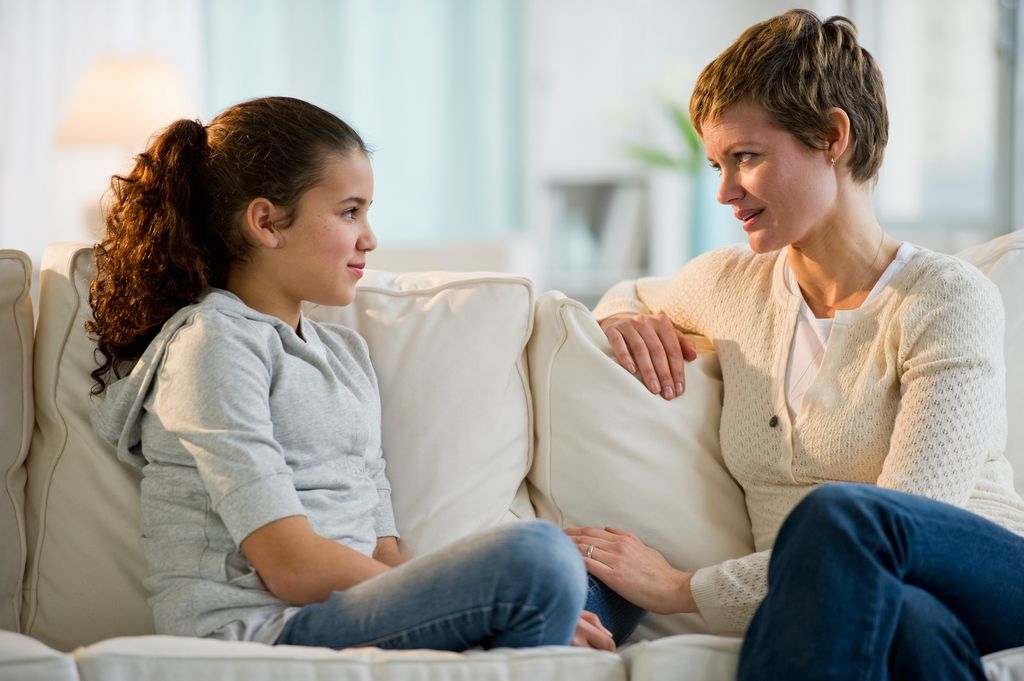 Madre hablando tranquila en el sofá con su hija preadolescente