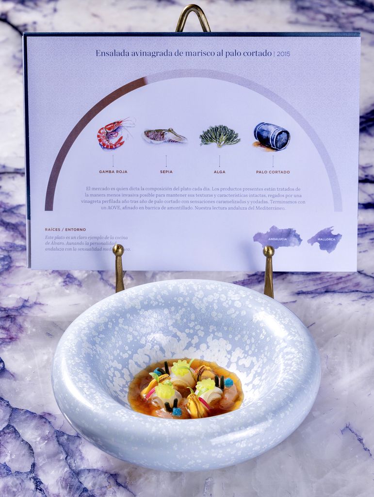 Los platos aparecen en mesa acompañados por bonitas cartelas ilustradas donde se explican detalles relacionados con las recetas. En este caso, un clásico de Voro: Ensalada avinagrada de marisco al Palo Cortado. 