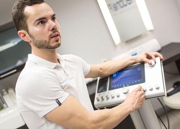 Hombre en clínica con uniforme blanco, operando un dispositivo médico.