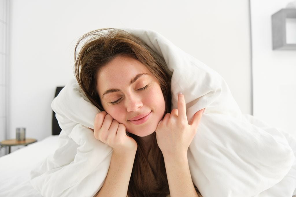 mujer abrigada con el edredón de la cama