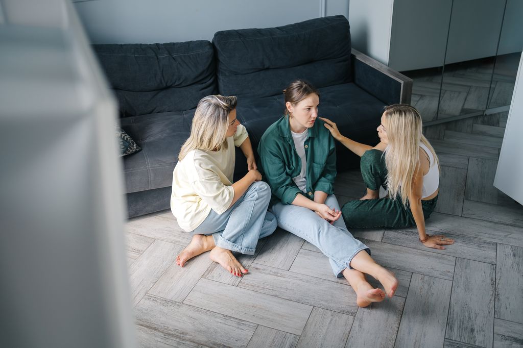 amigas hablando, sentadas en el suelo, ayudando a una de ellas con problemas