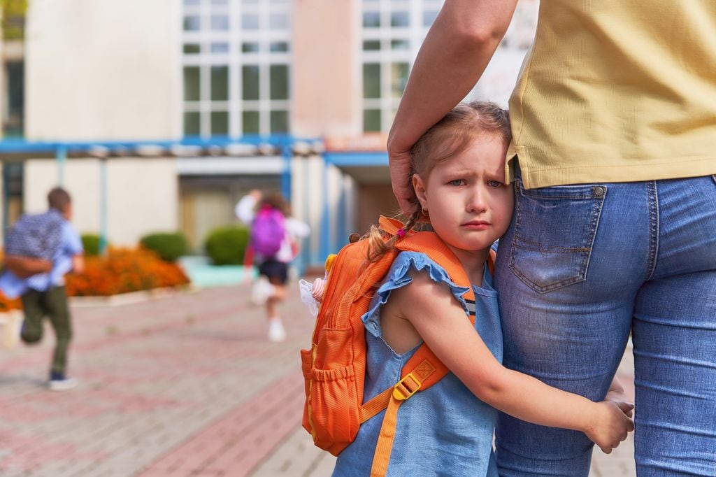 Hija pequeña llorando agarrada a la pierna de su madre por el primer día de cole