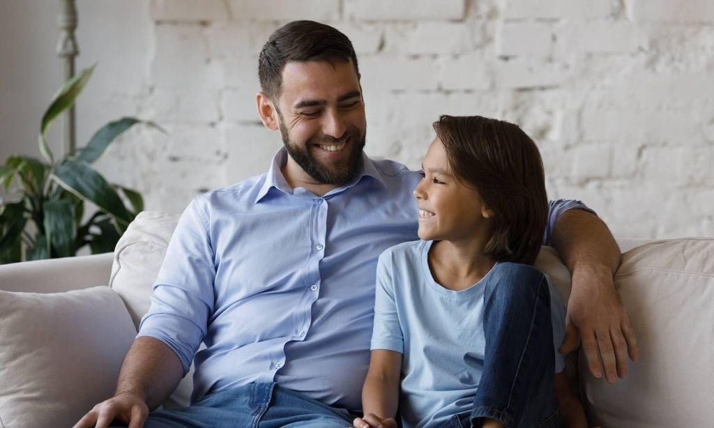 padre hablando con su hijo feliz sentados en el sof de su casa