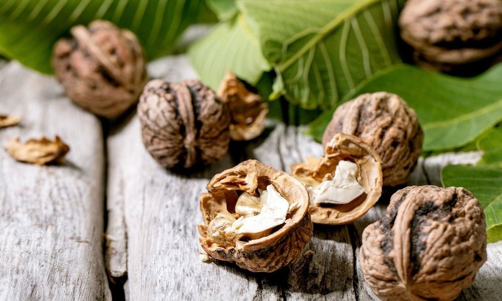 Organic walnuts. whole and broken. with green leaves of walnut tree over old wooden background. Close up