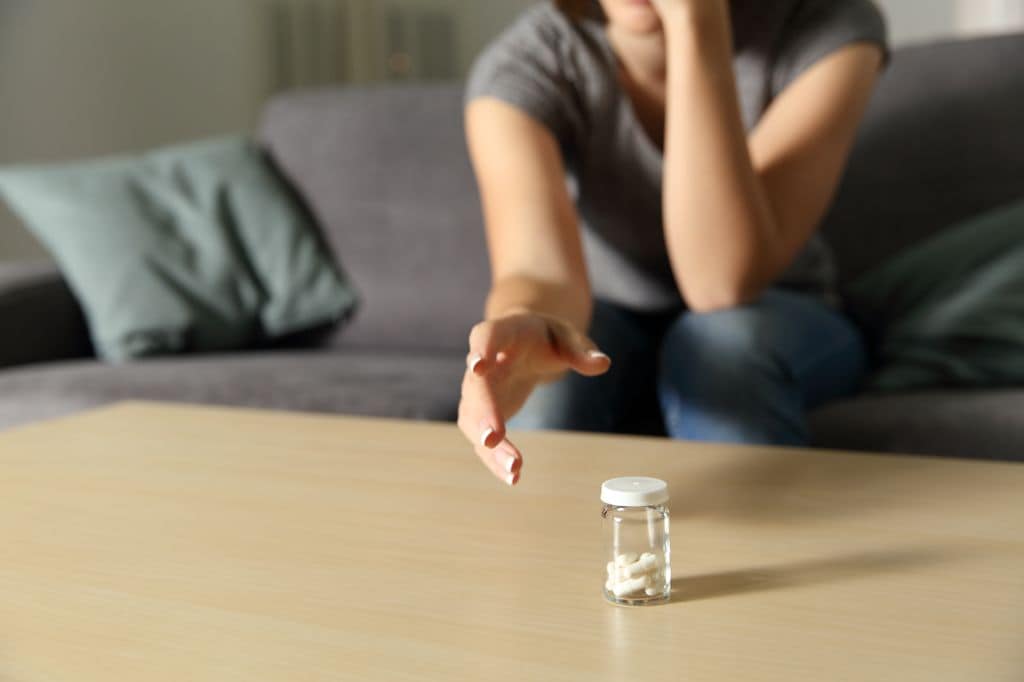 mujer cogiendo un bote de pastillas que hay sobre la mesa