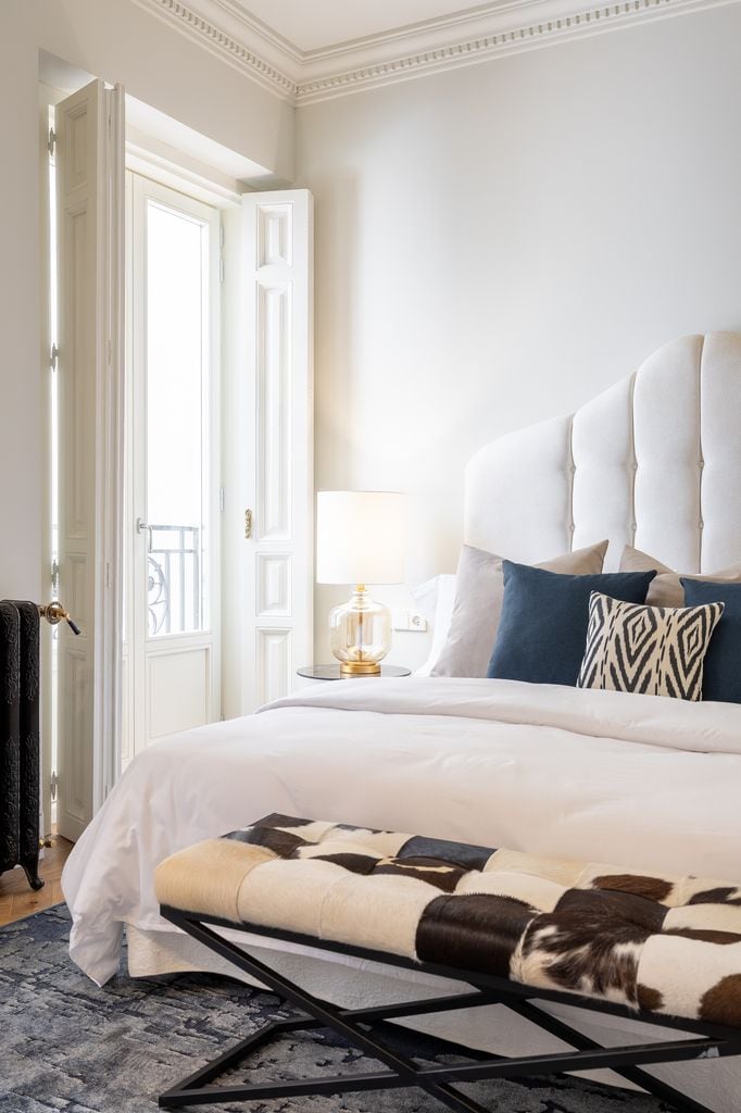 Dormitorio blanco con banco tapizado con piel de potro a los pies de la cama