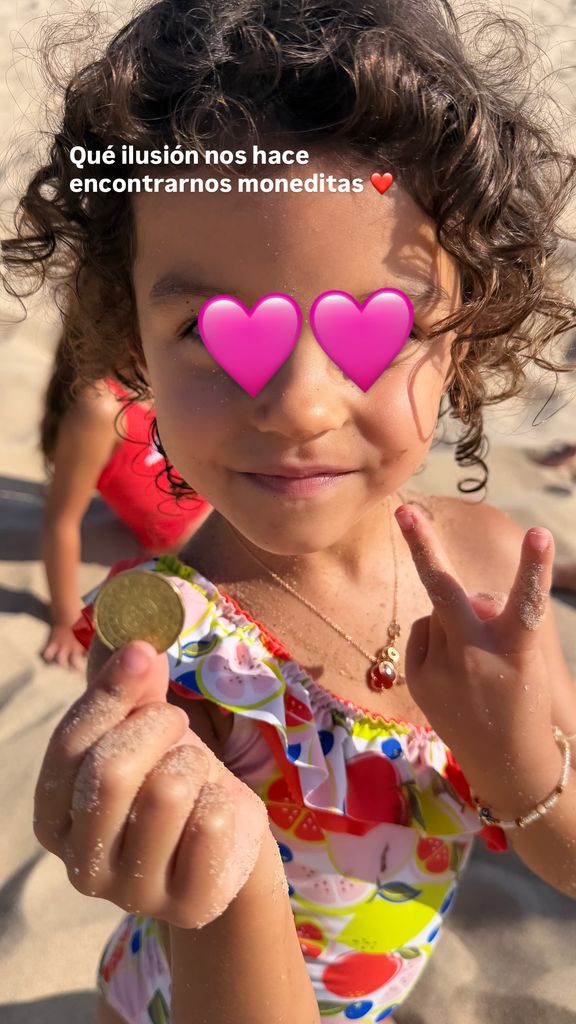Bella Esmeralda, de 4 años, le enseña a su madre la moneda que ha encontrado en la playa