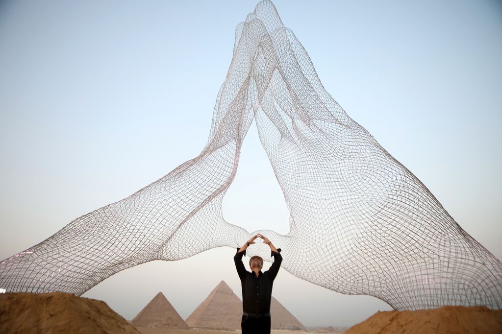 Lorenzo Quinn posa bajo su instalación titulada"Juntos", frente a las pirámides en la meseta de Giza