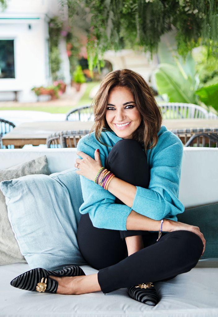 Mariló Montero posa con un precioso jersey azul de punto, abrazando las rodillas en un sofá del jardín de casa en Sanlúcar