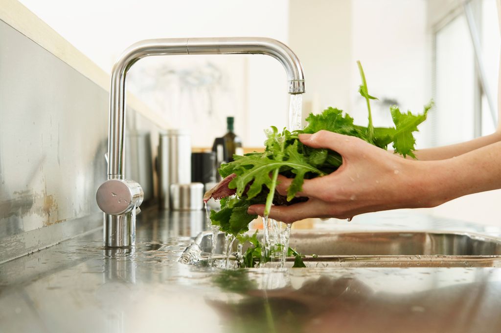 mujer lavando hojas de lechuga y otros brotes verdes bajo el grifo