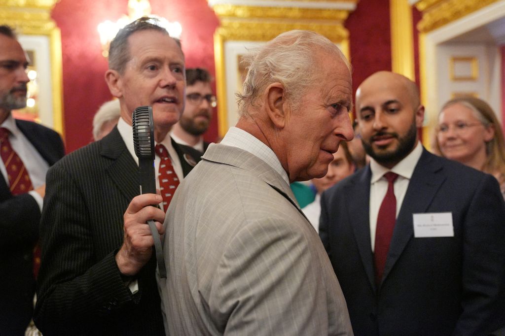 El vicealmirante Sir Tony Johnstone-Burt, jefe de la Casa del Rey, sostiene un pequeño ventilador portátil para el rey Carlos III durante la recepción de la Semana del Clima de Londres, organizada por el Departamento de Seguridad Energética y Cero Emisiones Netas (DESNZ), en el Palacio de St. James, en Londres, el 24 de junio de 2026