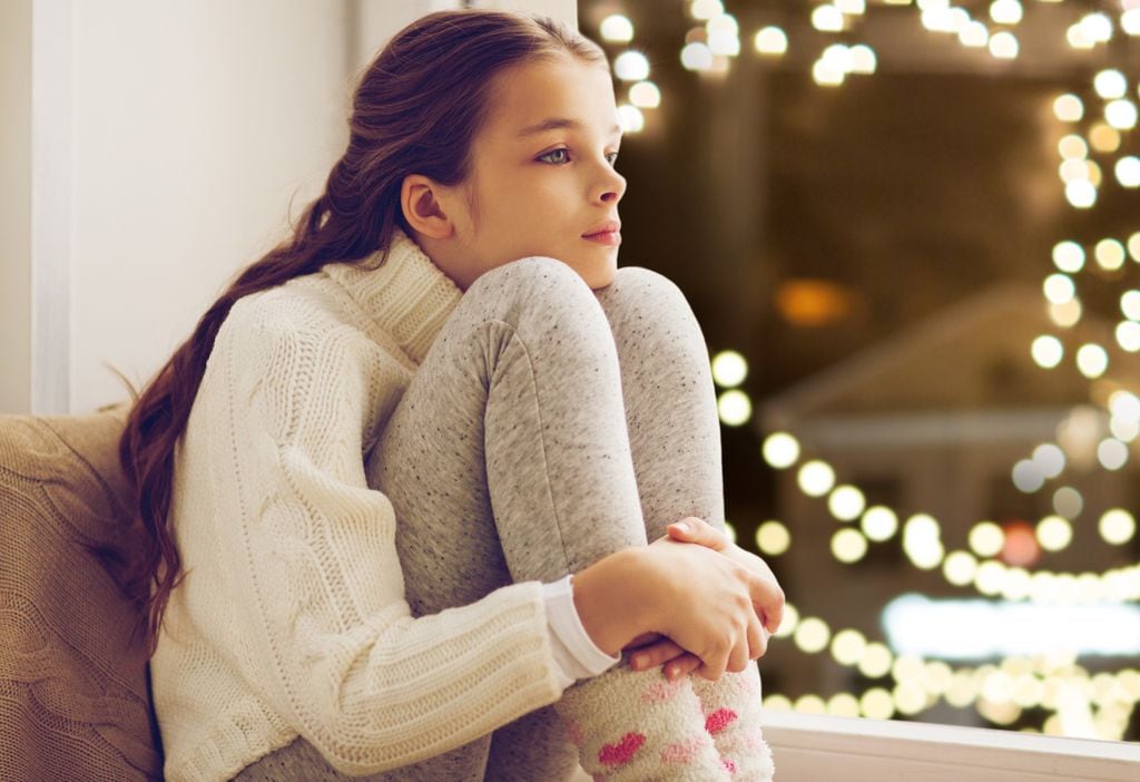 Adolescente triste en Navidad al lado de una ventana