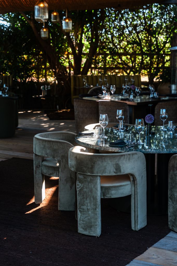 Restaurante al aire libre con mesas y sillas de terciopelo, ambientado con lámparas colgantes.