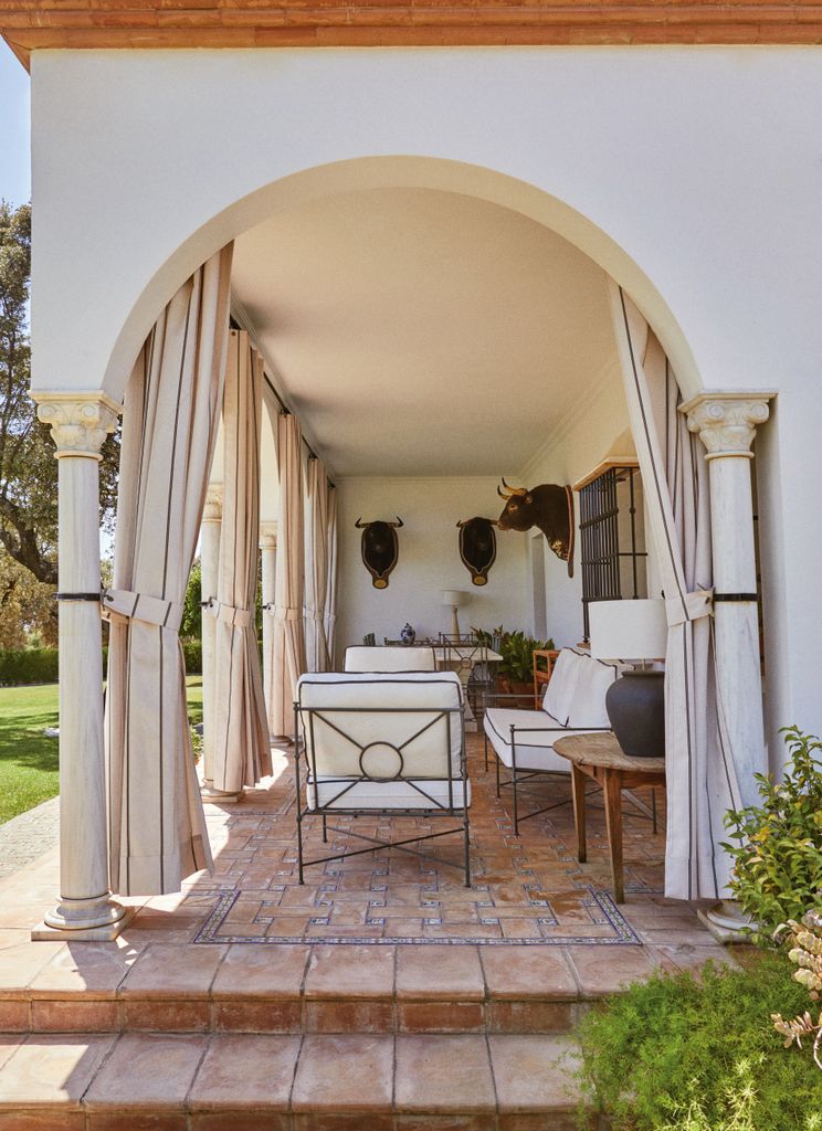 El espectacular porche de la finca sevillana de Roca Rey, una estancia relajada, con muebles tradicionales en blanco y madera y cortinas para separar espacios y proteger del sol