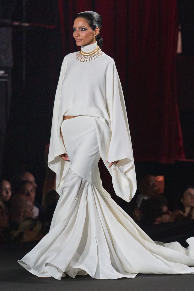Modelo en pasarela con vestido blanco de mangas anchas y escote alto.